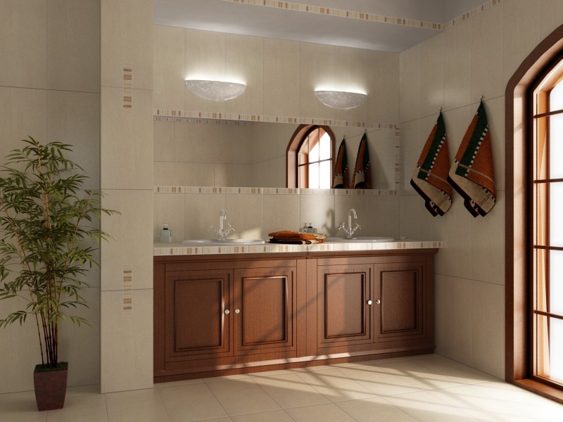 Jasna łazienka z brązowymi akcentami: drewniana szafka pod umywalką z marmurowym blatem, lustro z oświetleniem, beżowe płytki z dekoracyjnym paskiem, okno z łukiem i doniczkowa roślina.